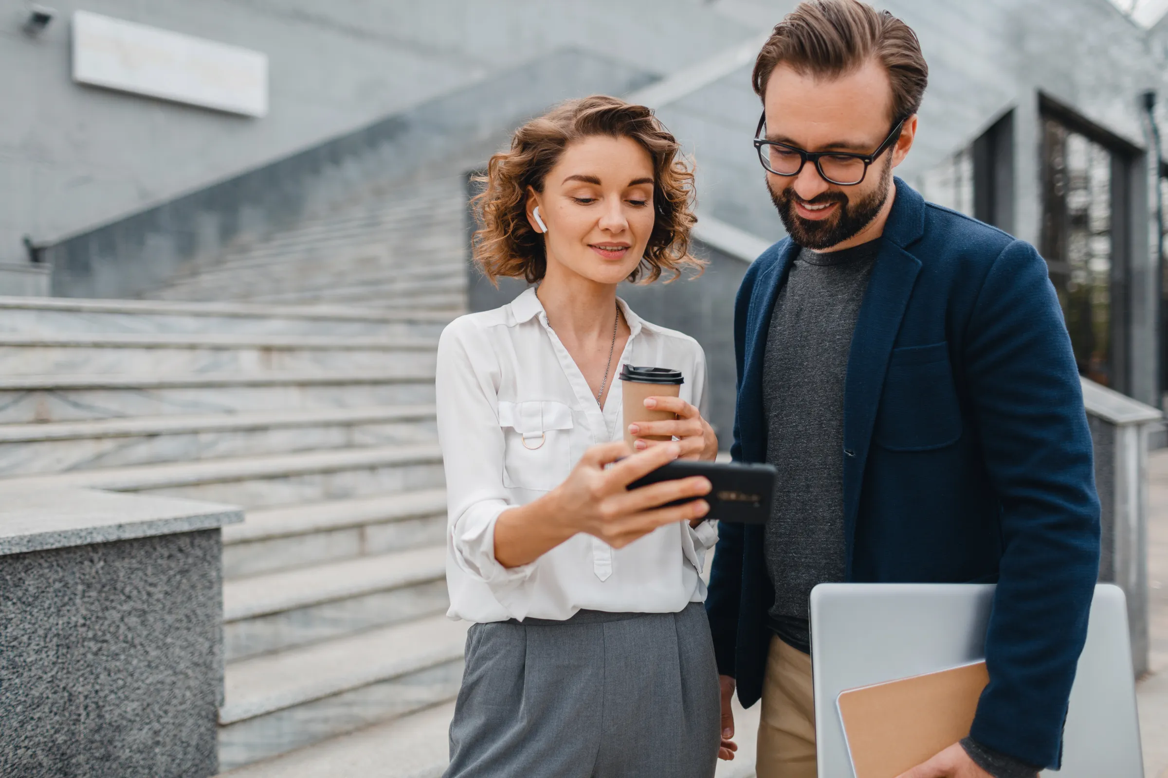 Twee collega's bekijken samen een rapport op een smartphone, buiten in de stad