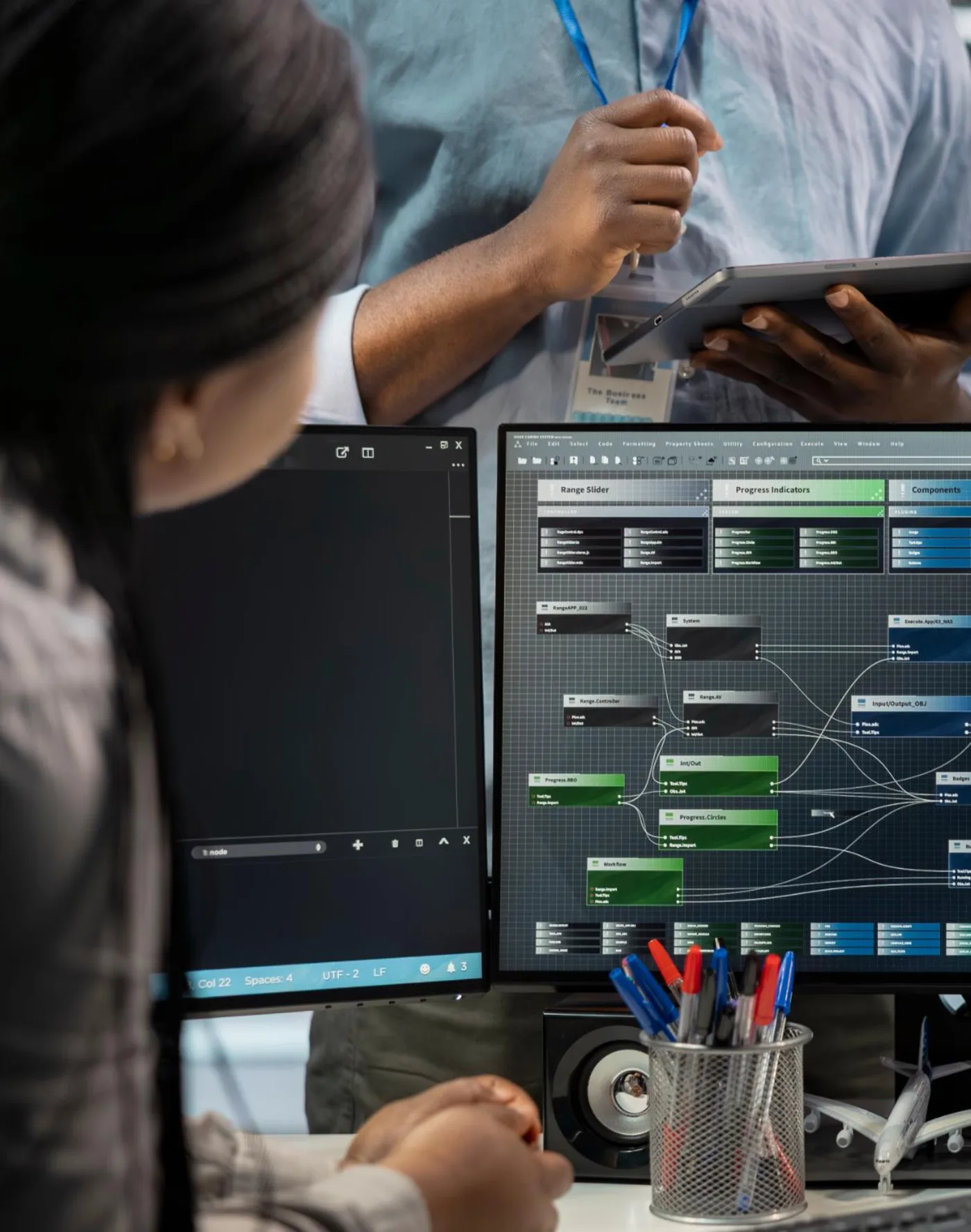 Over de schouder meegekeken naar een scherm met een workflow in blokken en verbindingen, terwijl een collega ernaast met een tablet meekijkt.